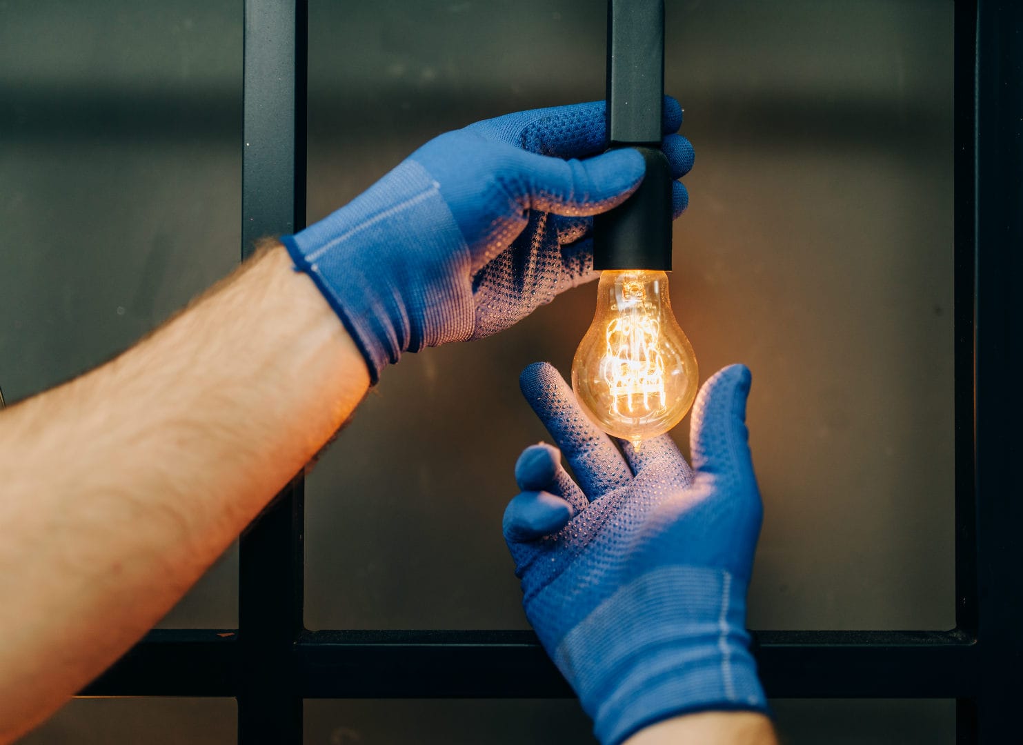 Two hands with blue gloves screwing on a light bulb.