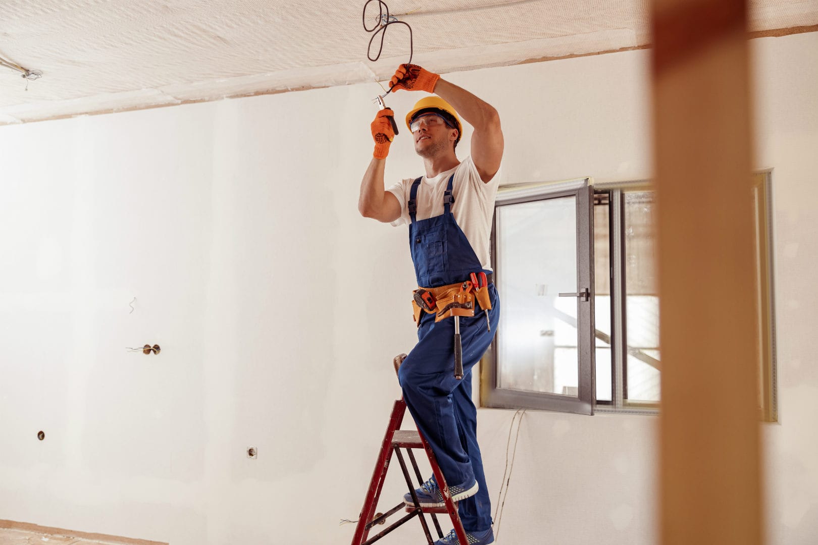 Electrician on a ladder inside a home reaching toward the cieling.